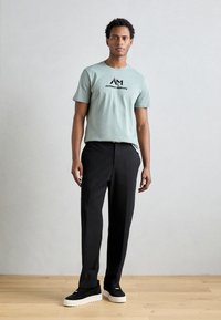 Lichtblauwe katoenen t-shirt met zwart logo, gecombineerd met zwarte op maat gemaakte broek en zwarte sneakers met witte zolen. Gladde textuur, casual pasvorm.
