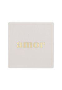 Vit fyrkantig platta med ordet "amor" i guldfolierade bokstäver centrerat på en enkel bakgrund.