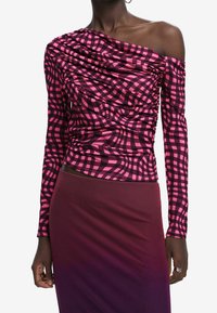 Pitkähihaiset paita, jossa on vaaleanpunainen ja musta ruudullinen kuvio, roikkuva muotoilu ja olkaimeton kaula-aukko, yhdistettynä yksiväriseen värigradientti-hameeseen.