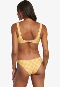 Bikini giallo e rosa a scacchi con spalline larghe, schiena a forma di scoiattolo e chiusura con gancetto, caratterizzato da una texture liscia e un design minimale.