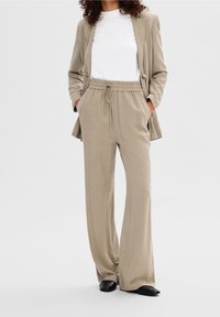 Béžové sako z lněné směsi s bílým tričkem pod ním, doplněné béžovými širokými kalhotami s elastickým pasem a stahovací šňůrkou.