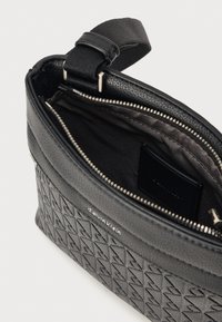 Calvin Klein svart lærveske med preget geometrisk mønster, glidelås, stoffforing, innvendig kortlomme, stiv rektangulær form.