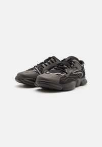 Black athletic shoes with textured gray accents, featuring a mesh upper, lace-up design, and rounded, cushioned sole for comfort.