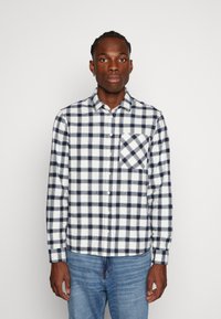 Camicia di flanella con bottoni, a quadri blu navy e bianchi, maniche lunghe, taschino sul petto e tessuto morbido.