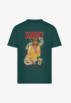 Zöld pamut póló, amelyen egy arany ruhás, gyöngyös díszítésű nő grafikai mintája látható, valamint a "SCARFACE" felirat piros betűkkel.