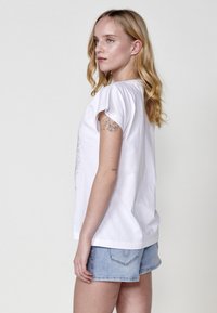 T-shirt en coton blanc à manches courtes roulées, avec un design graphique à l'avant. Associé à un short en denim bleu clair.