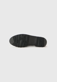 Black rubber shoe sole with textured grip patterns and a rounded toe. Features deep grooves in a zigzag design for traction.