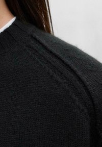 Pull en maille gris foncé avec un col côtelé et des coutures décoratives le long des épaules. Tissu doux et texturé.