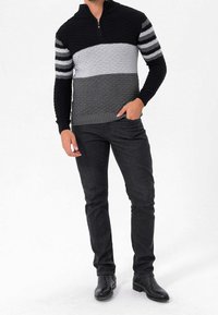 Black, gray, and light gray sweater with textured stripes, featuring a half-zip collar. Paired with dark jeans and black boots.