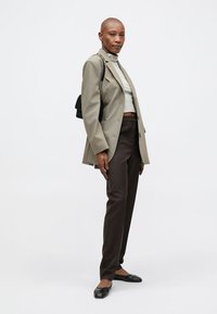 Dublán gombos olívazöld blézer, csíkos garbó, barna, szabott nadrág, fekete kézitáska és lapos fekete cipő. Simák a textúrák és a testhez álló dizájn.