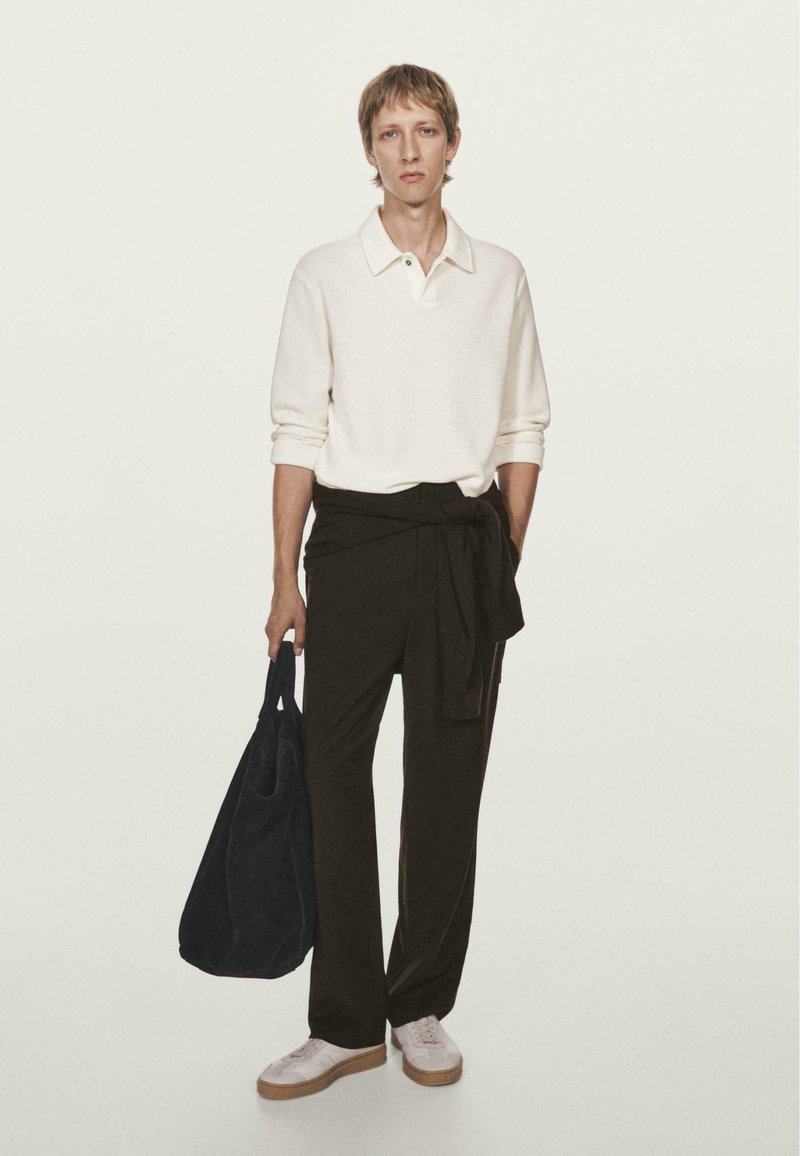 Polo bianco a maniche lunghe, pantaloni neri larghi con vita legata, borsa a spalla blu navy e sneakers bianche con suola beige. Design minimalista.