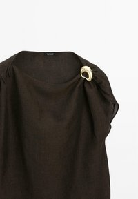 Haut en lin marron avec un décolleté large et un accent doré. Présente des détails froncés au niveau de l'épaule. Étiquette visible à l'intérieur du décolleté.