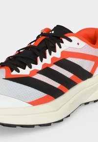 Λευκό και πορτοκαλί αθλητικό παπούτσι με μαύρα κορδόνια και τρεις μαύρες ρίγες στα πλάγια, με μαλακή σόλα και διαπνέον διχτυωτό υλικό.