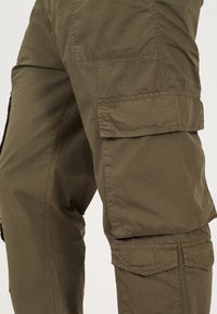 Παντελόνια cargo σε ελιά με ελαφρύ ύφασμα, διαθέτοντας πολλαπλές πλαϊνές τσέπες, ορατές ραφές και χαλαρή εφαρμογή.