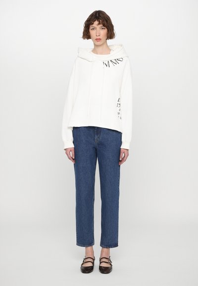 Λευκό φούτερ με τσέπη μπροστά, κορδόνια και μαύρο κείμενο στο στήθος. Συνδυάζεται με μπλε τζιν παντελόνι και μαύρα σανδάλια με λουριά.