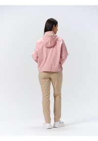 Rosa leichte Jacke mit Kapuze, leicht verkürztem Schnitt, kombiniert mit beigen Hosen und weißen Sneakers, von hinten gezeigt.
