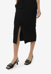 Sort midi-nederdel med en sideslids, glat stof og let tætsiddende form. Sammen med sorte åbne slingback-sandaler med dekorativ accent.