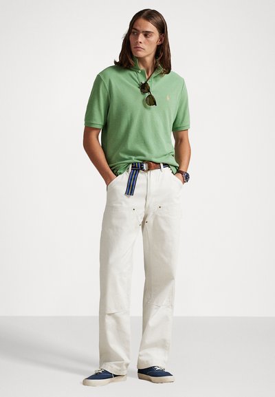 Zaļš kokvilnas polo krekls ar apkakli, baltas brīvas formas bikses un jūras bļodas stila apavi. Iekļauta svītraina jostas un saulesbrilles.