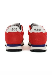 Scarpe sportive in suede rosso con accenti bianchi, dotate di una striscia blu sulla suola. Il tallone presenta l'anno "1968" in caratteri in grassetto.