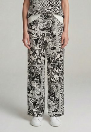 Person wearing black and white floral and geometric print wide-leg pants with white sneakers, standing against a plain background.