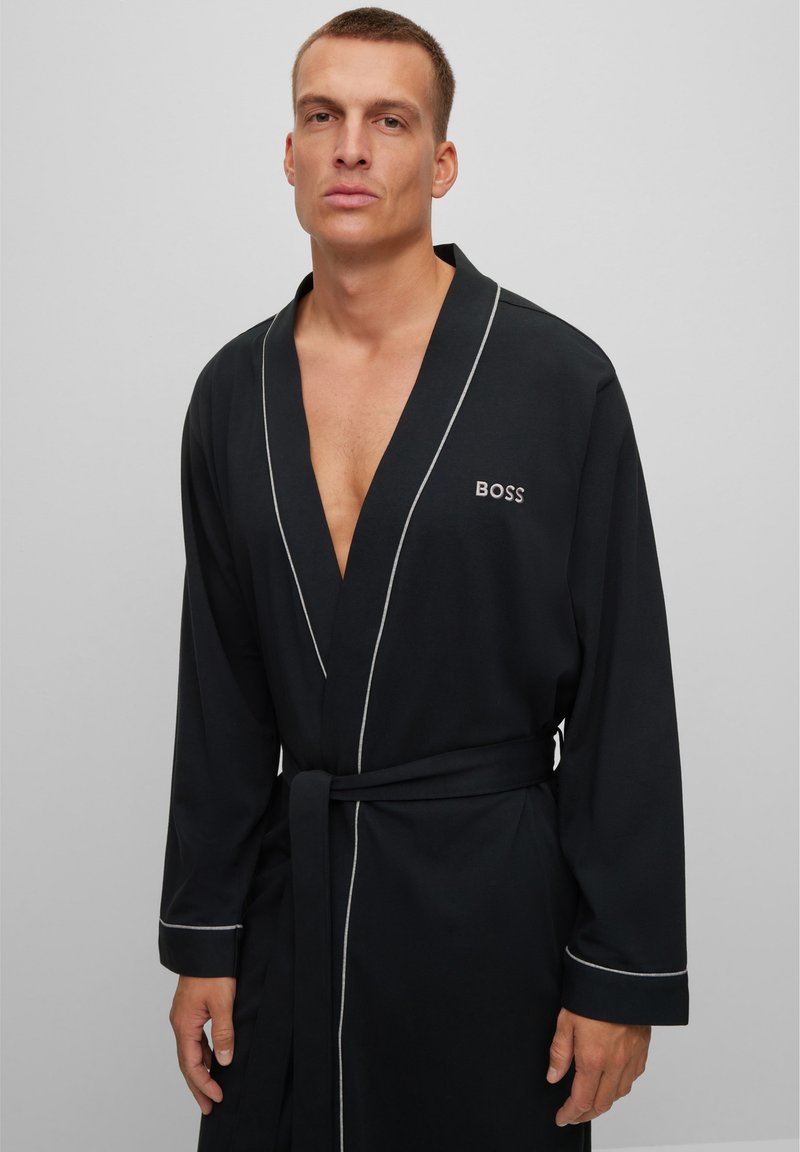 Accappatoio nero realizzato in morbido tessuto, con colletto a scialle, piping bianco a contrasto e cintura in vita, con un logo sul petto.