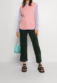 Rosa ribbad väst, lavendelfärgad långärmad skjorta, mörkgröna kordbyxor, svarta sandaler, och en ljusblå handväska med kedjehandtag.