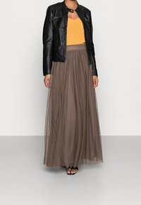 Black leather jacket with zip details, mustard yellow top, and a long, flowing brown sheer skirt. Sandals with a simple strap design.