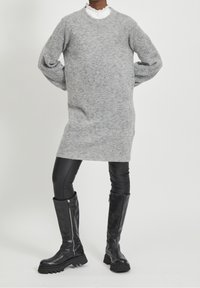 Vestito a maglione grigio con maniche lunghe, scollatura a coste e vestibilità comoda, abbinato a pantaloni in ecopelle neri e stivali alti fino al ginocchio.