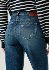 Blauwe spijkerbroeken van denim met een vervaagd uiterlijk, voorzien van twee achterzakken met contrasterende stiksel en een bruine leren logo patch op de taille.