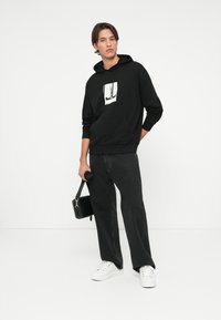 Felpa nera con grafica frontale, vestibilità comoda e polsini a costine. Abbinata a jeans neri a vestibilità ampia e sneaker bianche. Porta una piccola borsa nera.