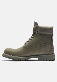 Bottine kaki à lacets avec col matelassé et semelle en caoutchouc robuste, conçue pour une utilisation en extérieur ou décontractée.