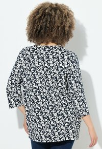 Námořnická modrá blůza s bílým květinovým vzorem, tříčtvrteční rukávy a volnější střih, vyrobená z měkkého materiálu s hladkým povrchem.