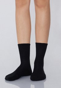 Czarne bawełniane skarpetki za kostkę z żeberkowym mankietem, dopasowanym krojem i gładką teksturą, spoczywające na nagich nogach na neutralnym tle.