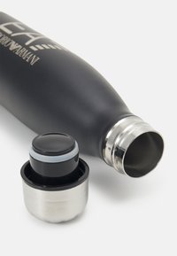 Bouteille d'eau en acier inoxydable, finition mate noire, forme élancée, comprend un bouchon vissé noir et argent avec un accent en caoutchouc doux.