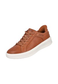 Zapatilla de cuero marrón con punta redondeada, suela de goma blanca y cordones prominentes. Presenta una lengüeta con marca y detalles de costura sutiles.