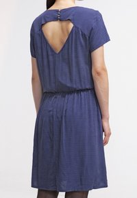 Mörkblå klänning med vita prickar, korta ärmar, elastisk midja och en nyckelhålsstängning bak med knappar. Slät tygtextur.