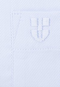 Jasnoniebieska tkanina z delikatnym wzorem w paski. Posiada haftowane logo na kieszeni, z gładkim, teksturowanym wykończeniem i starannym przeszyciem.