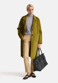 Cappotto di lana verde oliva, dolcevita grigio, pantaloni beige, borsa a tracolla nera in pelle e scarpe flat nere con dettagli a fascia. Elementi di design semplici.
