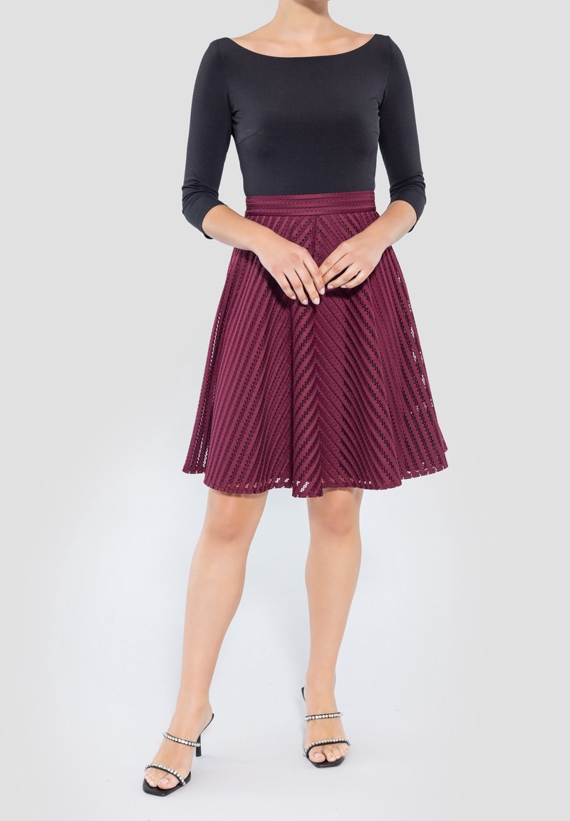 Blusa negra de manga larga combinada con una falda en A color burdeos que presenta patrones diagonales texturizados. El conjunto se completa con sandalias de tacón negras.