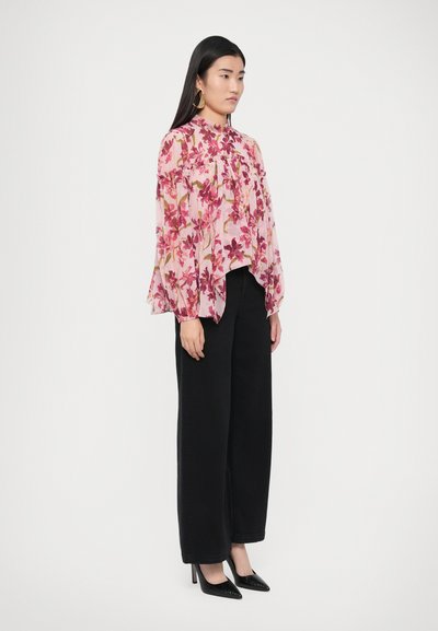 Blouse florale en tissu rose transparent avec des motifs violets et verts, dotée d'un col montant et de manches amples, assortie à un pantalon large noir.