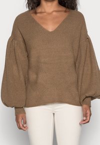 Pull en tricot marron avec un décolleté en V, texture côtelée et manches bouffantes ; terminé par une coupe décontractée et un ourlet incurvé.