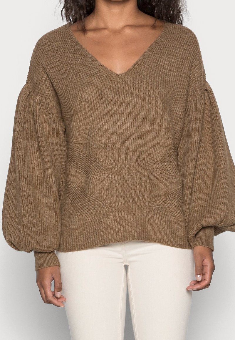 Pull en tricot marron avec un décolleté en V, texture côtelée et manches bouffantes ; terminé par une coupe décontractée et un ourlet incurvé.