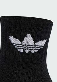 Calzino di cotone nero con logo Adidas lavorato a maglia bianco, che include un design a tre foglie e due strisce orizzontali vicino al bordo.