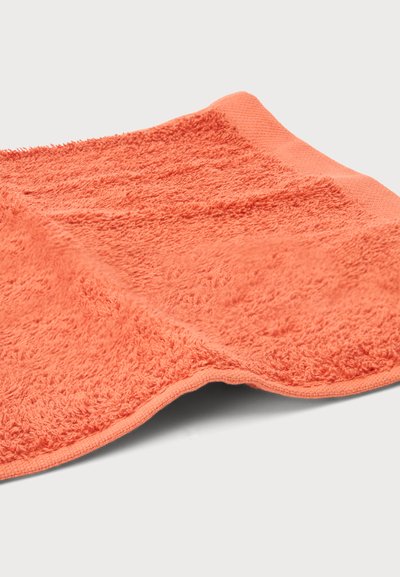Gant de toilette orange corail doux avec des boucles texturées et une bordure lisse, posé à plat sur une surface claire.