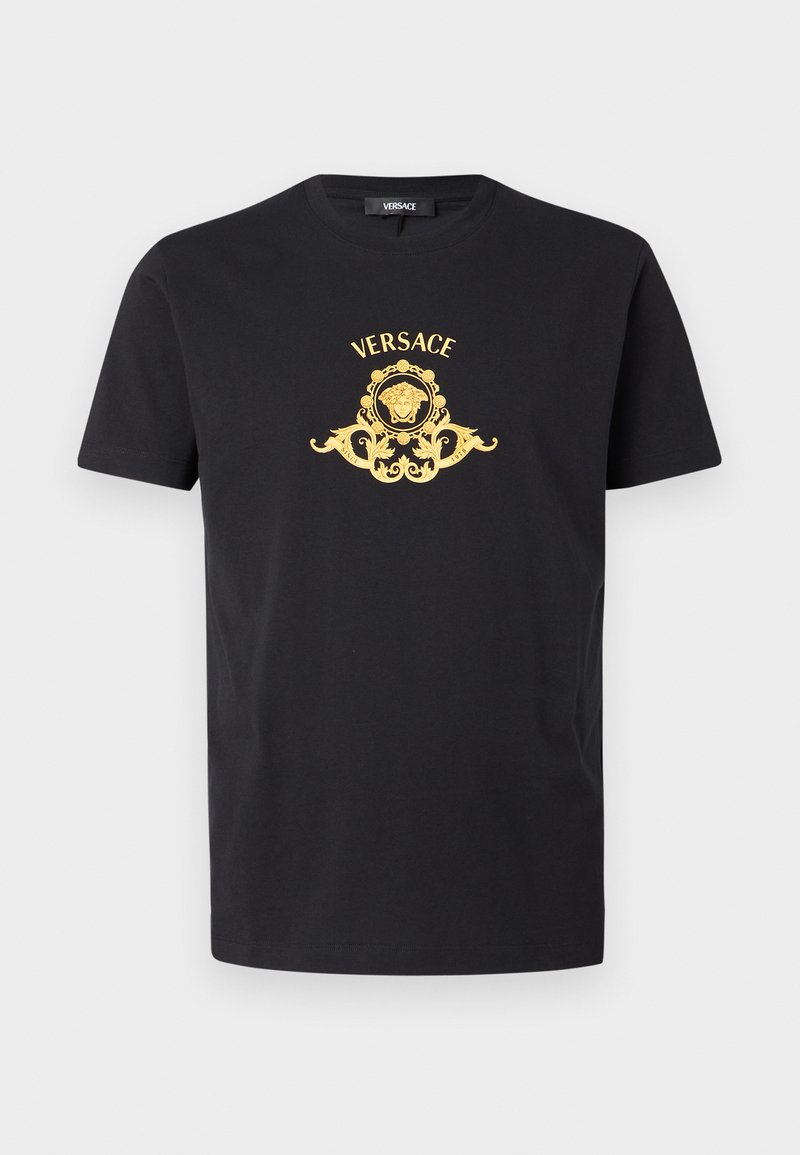 Sort bomuldst-shirt med et gyldent grafisk design, der viser et løvehoved, ornamentale detaljer og "Versace"-logoet over designet.