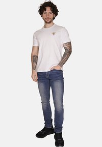 T-shirt bianco a maniche corte con piccolo logo ricamato, abbinato a jeans in denim blu e sneaker nere, con un design slim-fit.