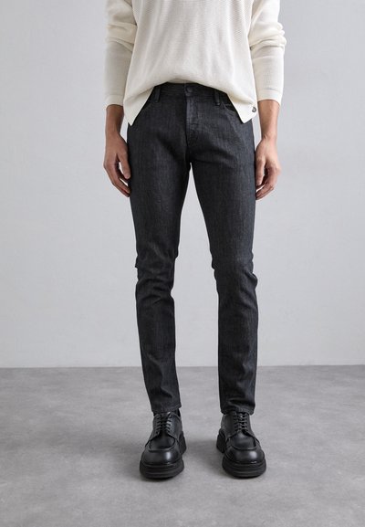 Ciemnojeansowe slim-fit spodnie o gładkiej fakturze, zestawione z czarnymi skórzanymi butami na sznurówki. Na górze biała sweterkowa bluzka o prążkowanej fakturze.