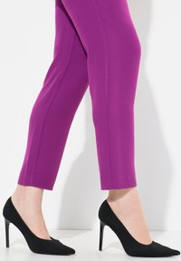 Pantaloni a lunghezza caviglia viola aderenti in un tessuto elastico abbinati a scarpe con tacco alto nere texturizzate, con punte appuntite e tacchi snelli.