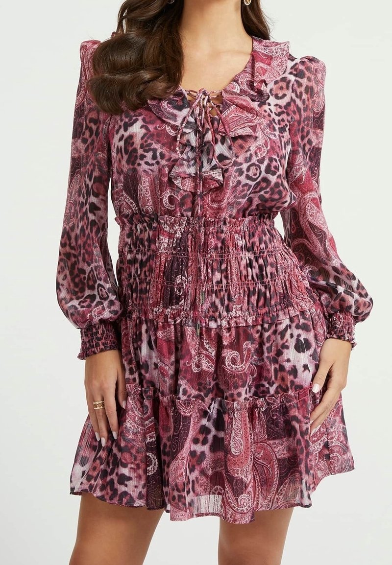 Femme portant une robe courte rose à manches longues avec des motifs léopard et paisley, un col à volants et une taille smockée.