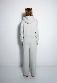 Jasnoszara, krótka bluza z kapturem, zestawiona z luźnymi spodniami o prostych nogawkach. Gładka faktura i minimalistyczny design bez wzorów.